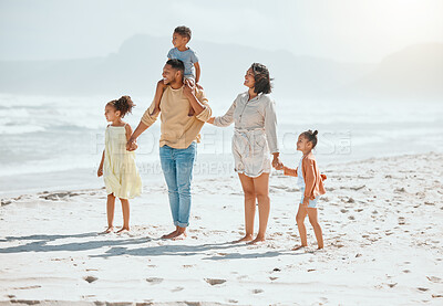 Happy mixed race family with three children holding hands and walking along the beach and looking at the view together. Loving parents with two daughters and son having fun and spending time while on vacation