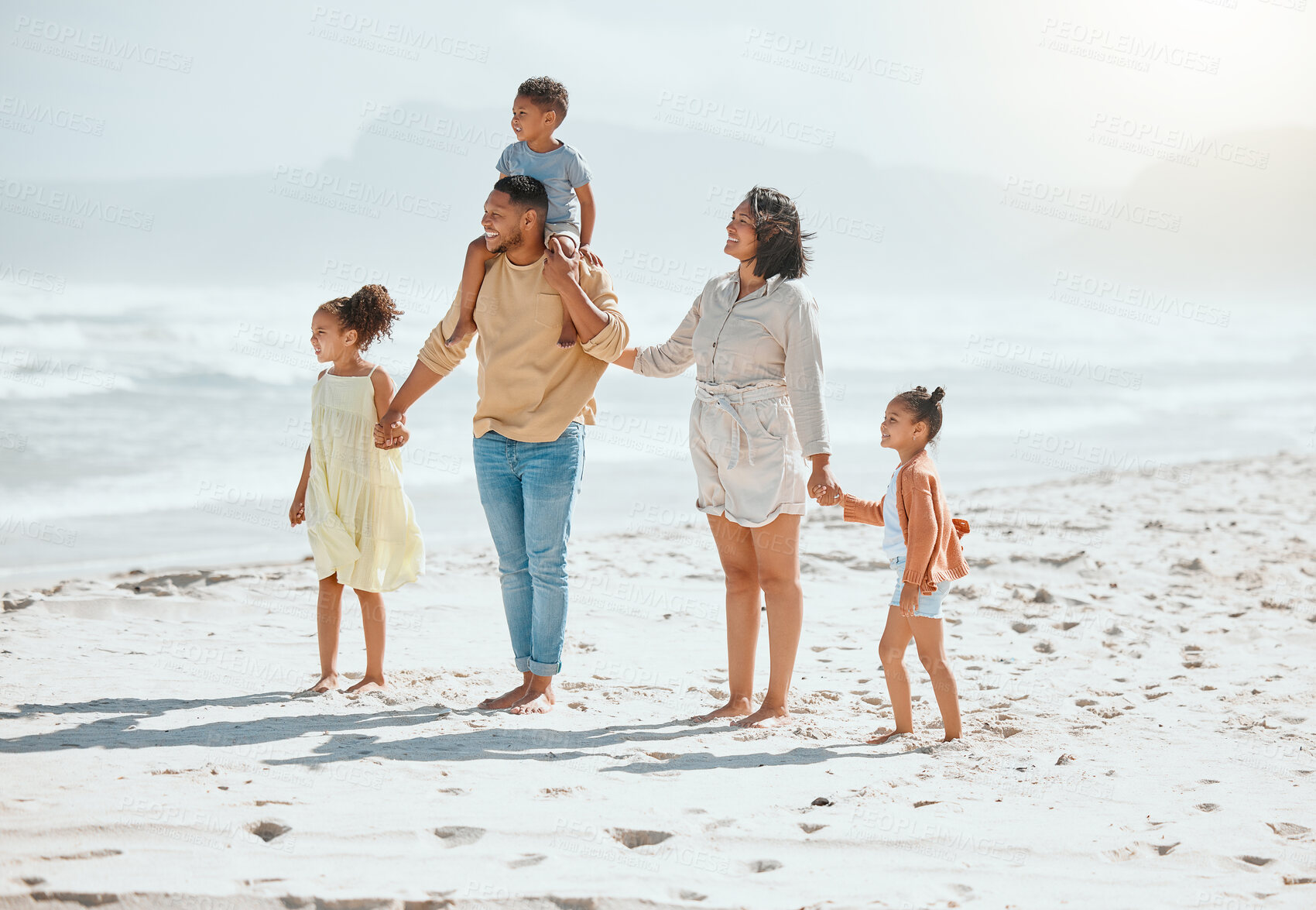 Buy stock photo Happy mixed race family with three children holding hands and walking along the beach and looking at the view together. Loving parents with two daughters and son having fun and spending time while on vacation