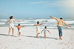 Rear view of a playful mixed race family with three children running on the beach with arms outstretched. A big family spending time and enjoying holiday by the sea