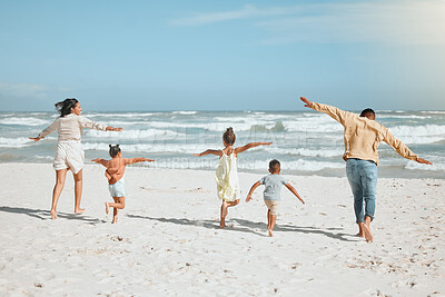 Rear view of a playful mixed race family with three children running on the beach with arms outstretched. A big family spending time and enjoying holiday by the sea