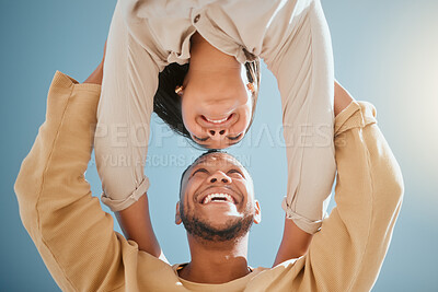 Happy young mixed race couple facing each other while standing with their hands on each others shoulders and smiling against a blue sky, from below