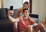 Happy young caucasian couple sitting together and taking selfie with smartphone. Young man holding mobile phone to take picture while sitting between girlfriends legs