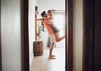 Happy young boyfriend holding girlfriend in arms as he lifts her up while they look into each others eyes and share intimate moment. Romantic young couple hugging and touching noses while enjoying passionate dance at home