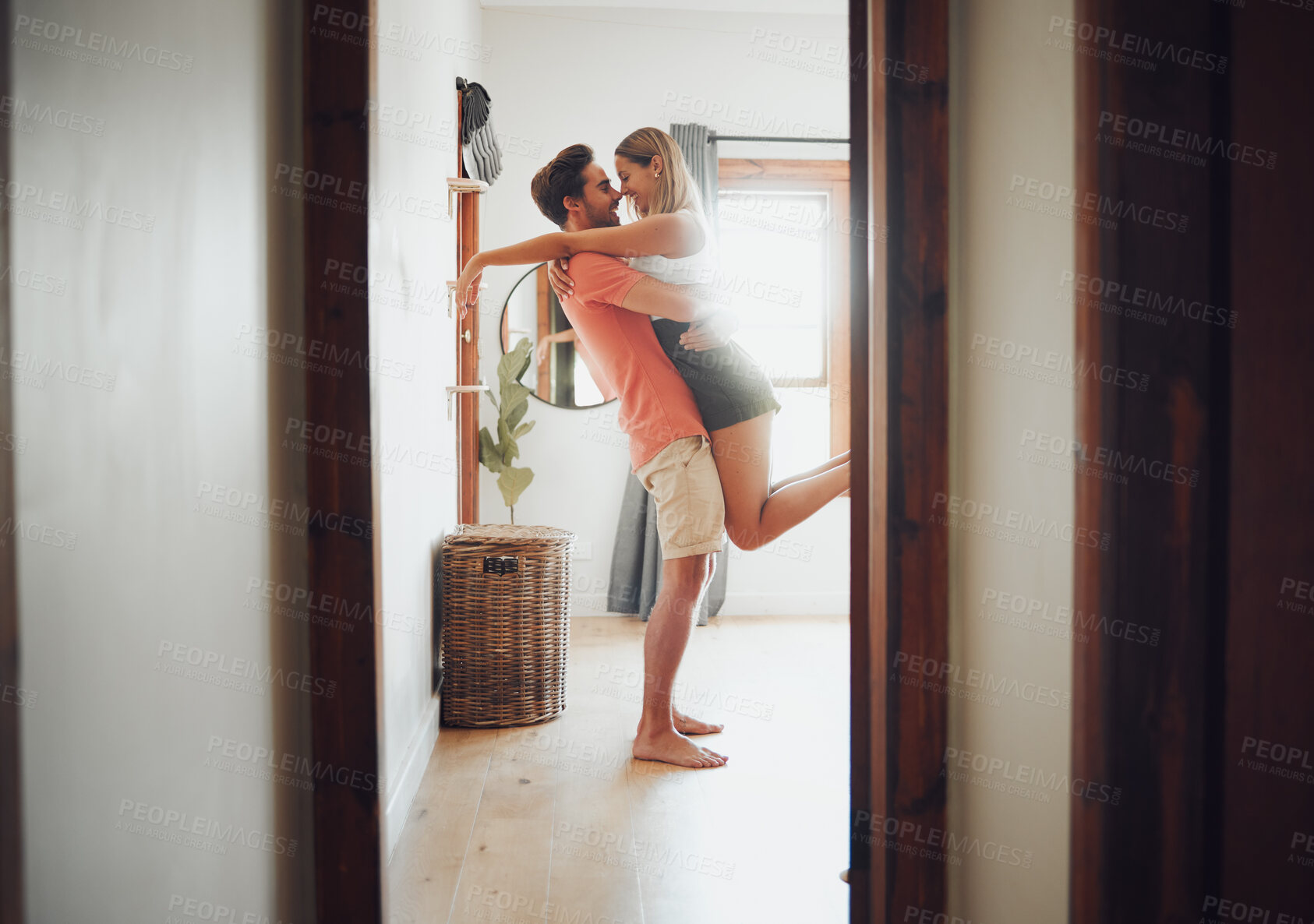 Buy stock photo Happy young boyfriend holding girlfriend in arms as he lifts her up while they look into each others eyes and share intimate moment. Romantic young couple hugging and touching noses while enjoying passionate dance at home