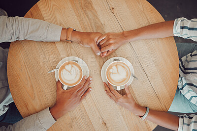 Close up of young couple in love holding hands with two cups of coffee on a table while sitting in a cafe. Male and female hands with hot cappuccino or espresso from above while on a date