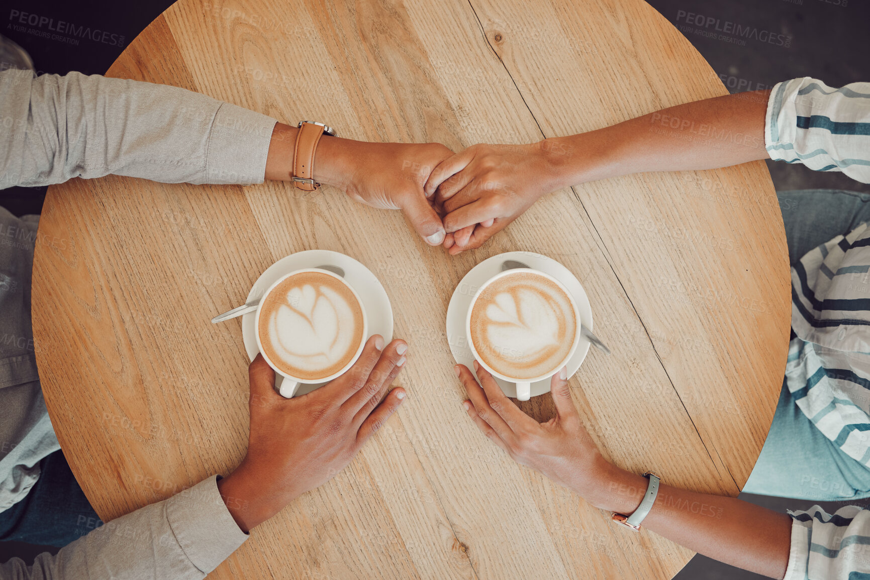 Buy stock photo Close up of young couple in love holding hands with two cups of coffee on a table while sitting in a cafe. Male and female hands with hot cappuccino or espresso from above while on a date