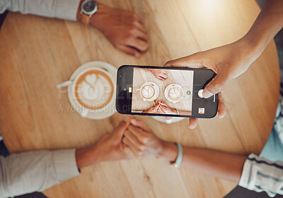 Close up of device screen while couple holds hands with two cups of coffee on a wooden table while taking a selfie on smartphone. Female and male hands on a table while on a date at a cafe