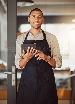 Businessman using a digital tablet in his cafe entrance. Bistro boss using an online app in the restaurant. Young small business owner using a wireless digital device in his cafe.