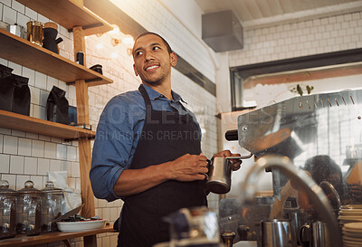 Mixed race barista steaming milk for coffee. Bistro worker frothing milk for a cup of coffee. Coffeeshop assistant holding a jug to froth milk for coffee. Cafe worker making coffee in the kitchen