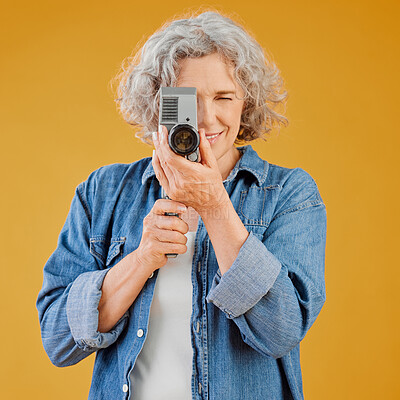One happy caucasian woman standing against a yellow background in a studio and taking a picture on a camera. Confident cheerful caucasian lady holding a camera and taking a photograph. Smile and pose