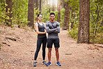 Full length portrait of a happy fit young couple standing with their arms crossed wearing sportswear and ready for a run in nature. Young female and male athlete out for a workout in pine forest