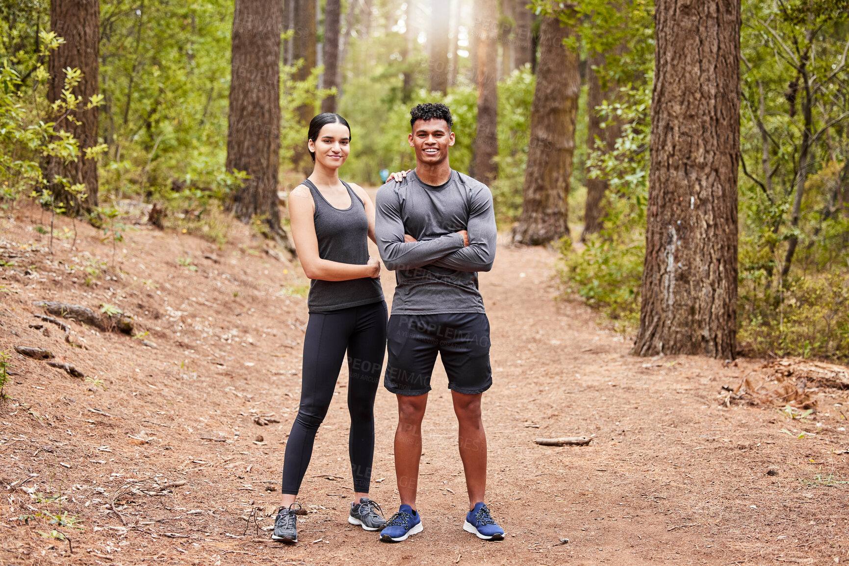 Buy stock photo Full length portrait of a happy fit young couple standing with their arms crossed wearing sportswear and ready for a run in nature. Young female and male athlete out for a workout in pine forest