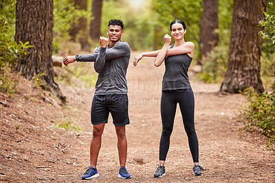 Portrait of a happy young male and female athlete stretching their arms before a run outside in nature. Two fit sportspeople doing warm-up exercises in pine forest on a sunny day