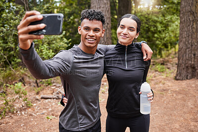 Happy young mixed race couple holding smartphone and taking selfie while out for a run in nature. Sporty young male and female in sportswear smiling while exercising outdoors in the forest. Achieving couple goals
