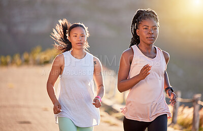 Buy stock photo Two focused young female athletes out for a run on a mountain road on a sunny day. Energetic young women running outdoors to help their bodies in shape and fit. Two sportswomen exercising together