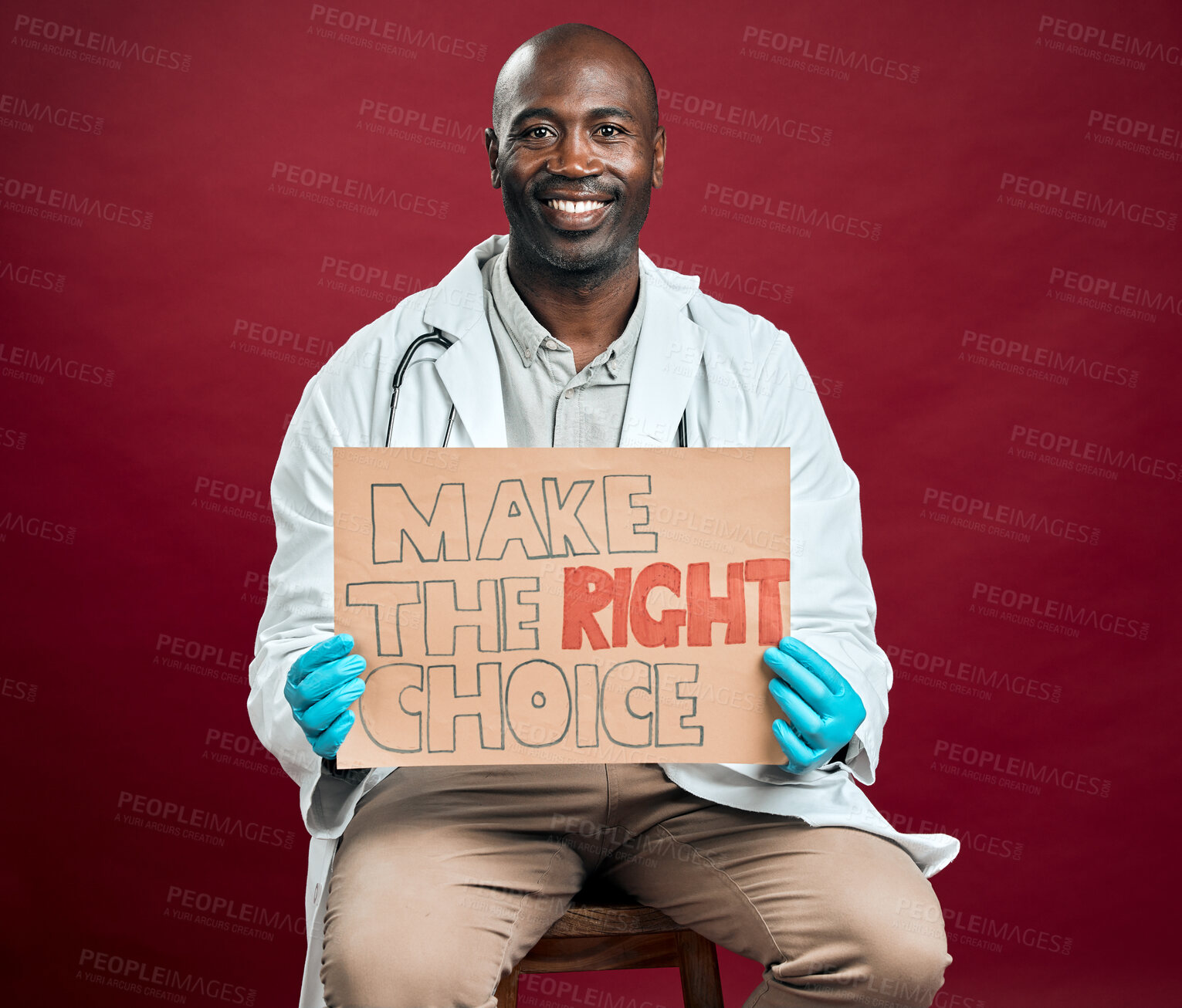 Buy stock photo African american covid doctor holding and showing poster. Portrait of smiling black physician isolated on red studio background with copyspace. Man promoting and encouraging corona vaccine on sign