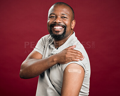 Buy stock photo African american covid vaccinated man showing arm plaster and smiling. Portrait of black man isolated against red studio background with copyspace. Model protected from corona with vaccine injection