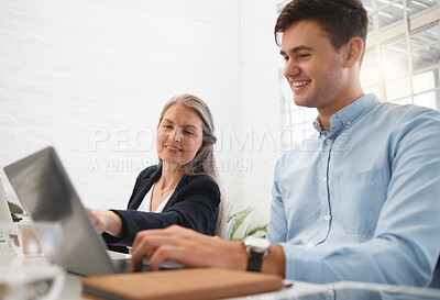 Two caucasian businesspeople working on a laptop together In an office at work. Mature businesswoman helping a colleague with work on a computer. Young businessman typing on a laptop while getting help from a coworker