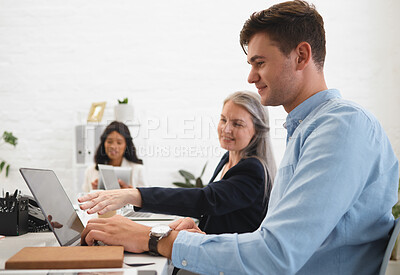 Mature caucasian businesswoman talking to a young male colleague while working on a laptop together at work. Boss showing an employee an idea on a laptop at work