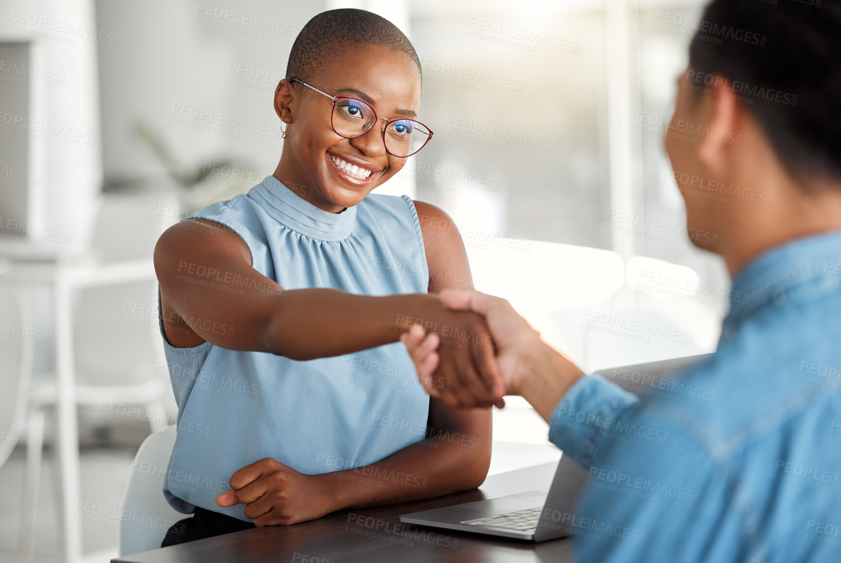 Buy stock photo Two cheerful businesspeople shaking hands in a interview together at work. Happy colleagues greeting with a handshake in an office. African american female boss promoting a male employee