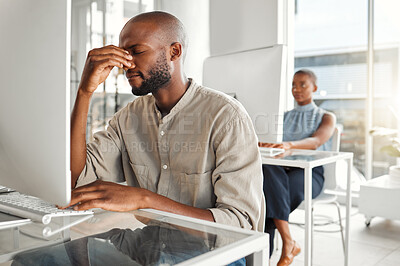 Young stressed african american businessman suffering from a headache while working on a desktop computer at work. One unhappy male businessperson suffering from anxiety while working on a computer at a desk in an office