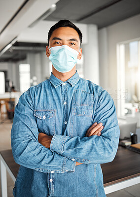 Buy stock photo Young asian businessman standing with his arms crossed and wearing a mask at work. One confident chinese male boss wearing a mask protecting from a virus and standing at work