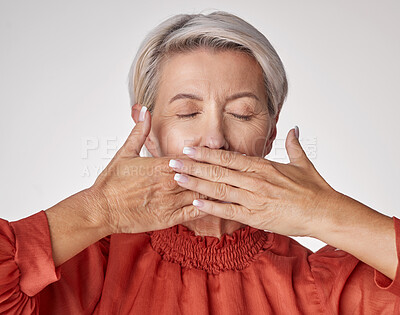 One mature caucasian woman isolated against a grey copyspace background in a studio with her hands covering her mouth. Ageing woman keeping secrets, not talking, hiding the truth, gossip