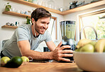 One fit young caucasian man using blender to make healthy green detox smoothie while wearing earphones in kitchen at home. Guy having fresh fruit juice to cleanse and provide energy for training. Wholesome drink with vitamins and nutrients