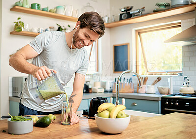One fit young caucasian man pouring healthy green detox smoothie from blender while wearing earphones in kitchen at home. Guy having fresh fruit juice to cleanse and provide energy for training. Wholesome drink with vitamins and nutrients