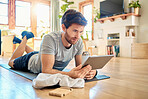 One fit young caucasian man using a digital tablet device while taking a break from exercise at home. Guy using fitness apps, browsing social media and watching online workout tutorials