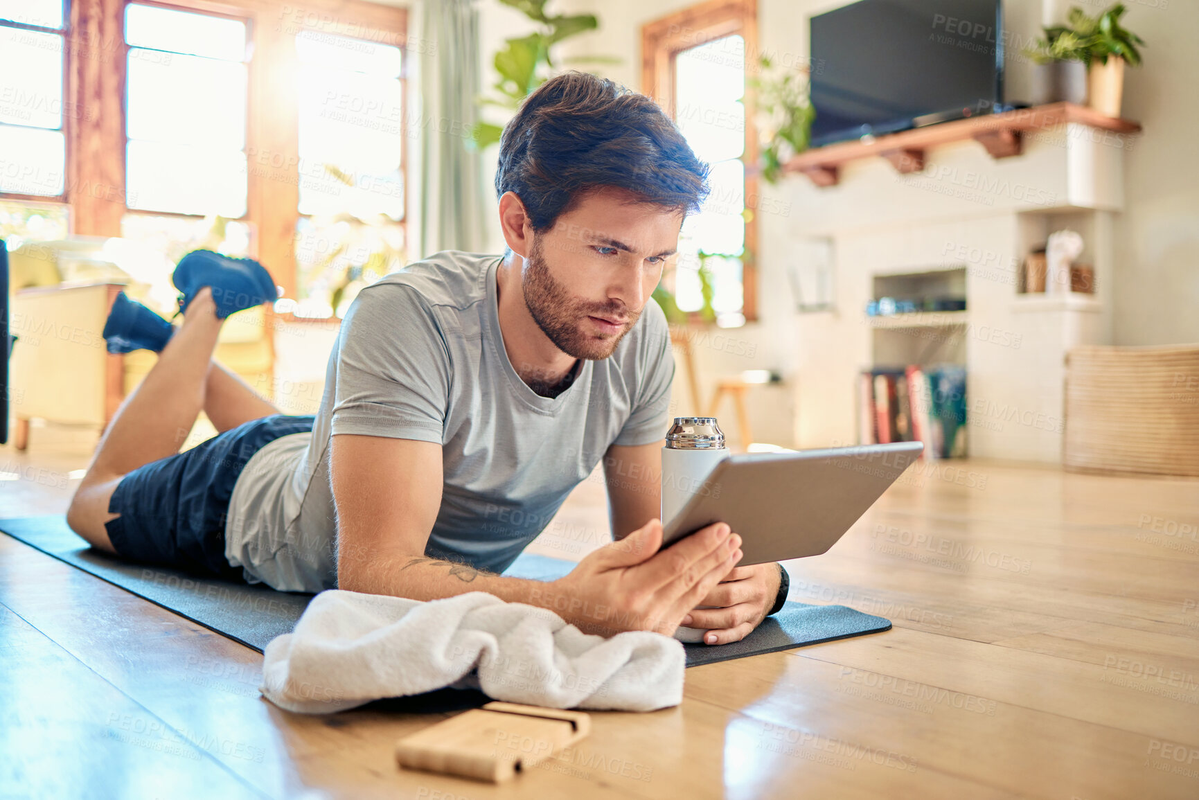 Buy stock photo One fit young caucasian man using a digital tablet device while taking a break from exercise at home. Guy using fitness apps, browsing social media and watching online workout tutorials