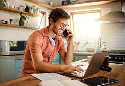 Young content caucasian businessman wearing glasses on a call using a phone while working on a laptop at home alone. Happy male businessperson smiling and talking on a cellphone while working in the kitchen at home