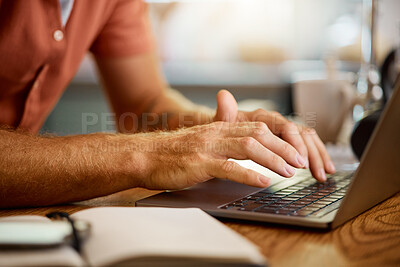 Man typing on a laptop while working from home alone. One businessperson working on a laptop and writing in a notebook while sitting at a table in the morning at home