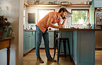 Fullbody of a young caucasian businessman on a call using a cellphone while working on a laptop and drinking coffee at home alone. Happy male businessperson talking on a cellphone while working in the kitchen at home