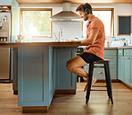 Fullbody of a young cheerful caucasian businessman wearing headphones and using a laptop at home alone. One joyful male businessperson smiling while working in the kitchen at home