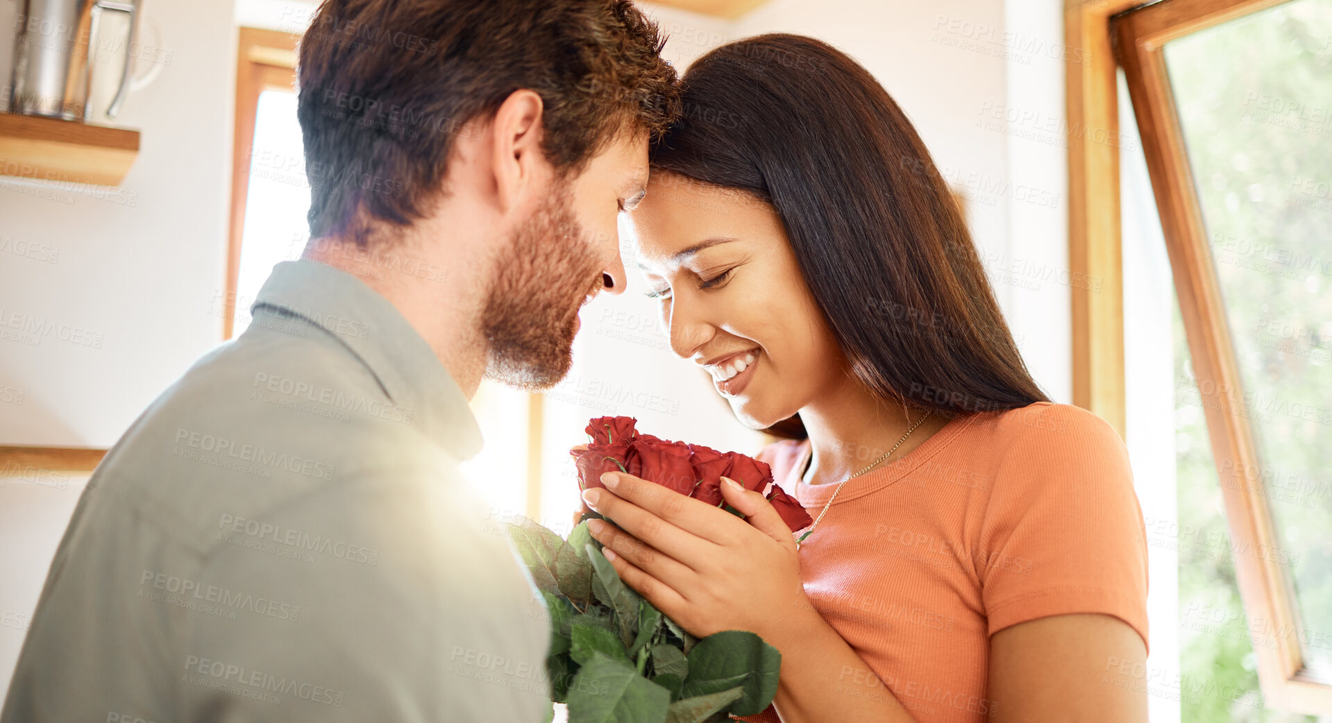 Buy stock photo Young content caucasian boyfriend giving his mixed race girlfriend a bouquet of flowers at home. Happy hispanic wife receiving roses from her husband. Interracial couple relaxing together at home