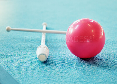 A red ball on the floor on a blue carpet. A set of drum sticks on a blue carpet next to a red sphere