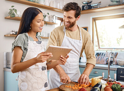 Buy stock photo Happy young interracial couple using digital tablet while cooking together at home. Young man cutting vegetables while wife reads online recipe. Couple preparing their first meal together