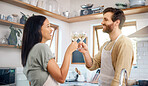 Young interracial couple sharing toast with wine glasses while wearing aprons and cooking together in kitchen at home. Young couple enjoying romantic homemade dinner for date night at home
