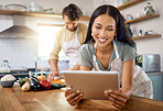 Close up of happy young woman browsing on digital tablet while her boyfriend cooks in the background. Young hispanic female searching for recipe to follow online while cooking at home with her husband