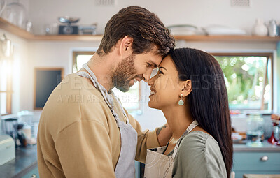 Buy stock photo Happy interracial couple touching foreheads while sharing romantic intimate moment at home while wearing aprons and cooking together. Young caucasian man and hispanic wife looking into each others eyes