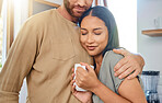 Loving young interracial couple spending time together at home. Young woman enjoying her morning coffee while boyfriend puts his arms around her. Young couple showing love and affection while enjoying morning leisure time