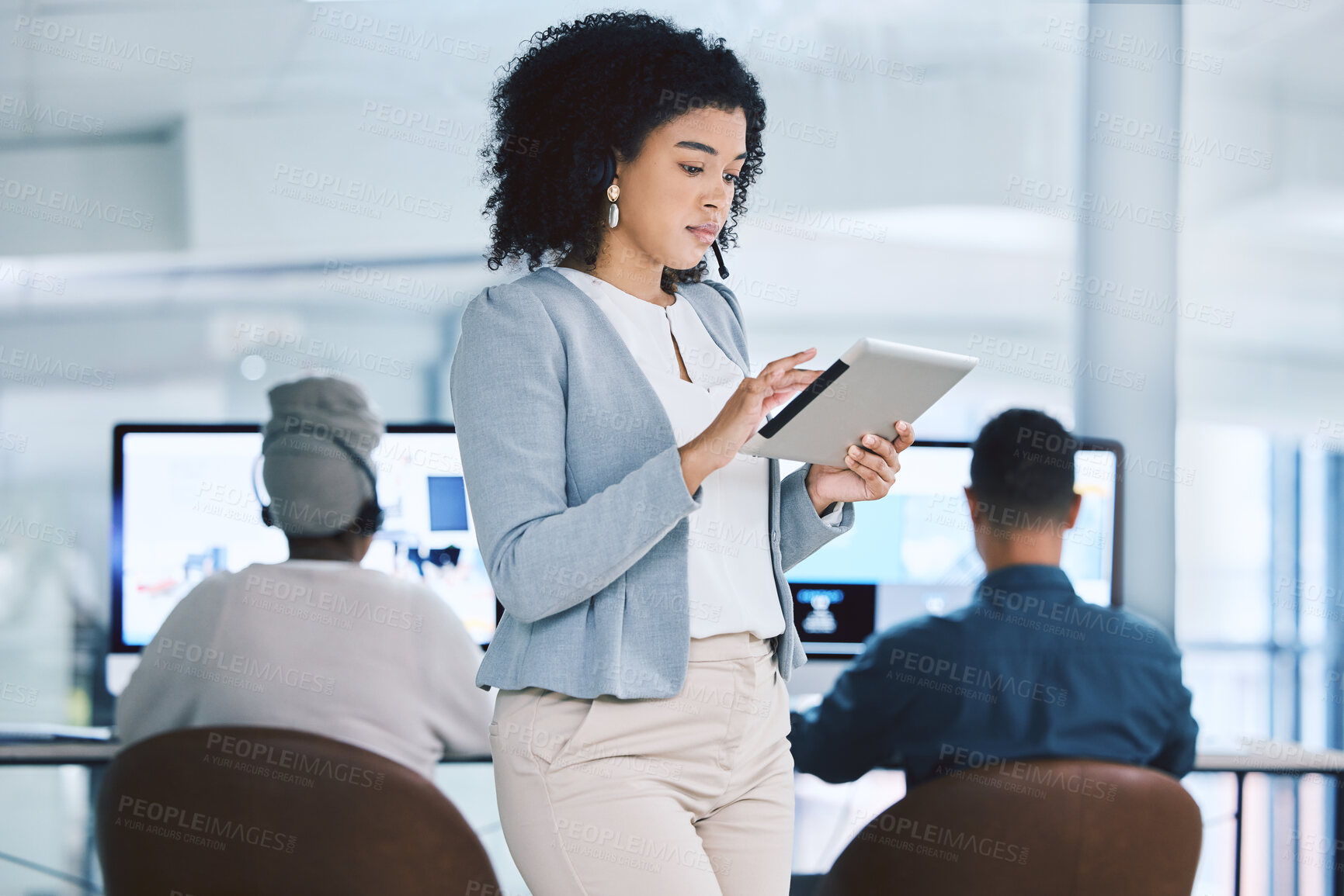 Buy stock photo Young mixed race businesswoman browsing on a digital tablet device while working in a call centre with her colleagues in the background. Serious manager and supervisor planning online with smart apps for customer service support