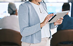 Closeup of mixed race businesswoman browsing on a digital tablet device while working in a call centre with her colleagues in the background. Female manager and supervisor planning online with smart apps for customer service support