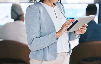 Closeup of mixed race businesswoman browsing on a digital tablet device while working in a call centre with her colleagues in the background. Female manager and supervisor planning online with smart apps for customer service support