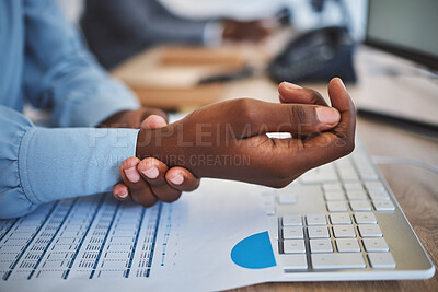 Closeup of one african american businesswoman suffering with aching wrist pain while working on a computer in an office. Black entrepreneur hurt with carpal tunnel syndrome disability. Feeling discomfort cramp in arm and hand