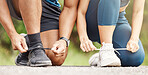 Closeup of a mixed race man and woman tying their shoelaces while exercising outdoors. Hands of two athletes fastening sneaker footwear for a comfortable fit and to prevent tripping while getting ready for cardio training workout or run at the park