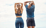 Fit young man and woman from the back stretching arms and triceps by pulling elbow with hands towards spine behind head while exercising outdoors. Two athletes doing warmup to prepare body and muscles for training workout or run