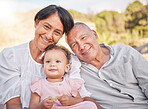 Happy mixed race grandparents sitting with granddaughter on a beach. Adorable, happy, hispanic baby girl bonding with grandmother and grandfather in a garden or park outside. Baby with foster parents
