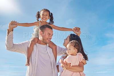 Buy stock photo A happy mixed race family of four enjoying fresh air at the beach. Hispanic couple bonding with their daughters while walking and carrying their daughters